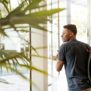 A college student with a backpack exits a campus building through glass doors.